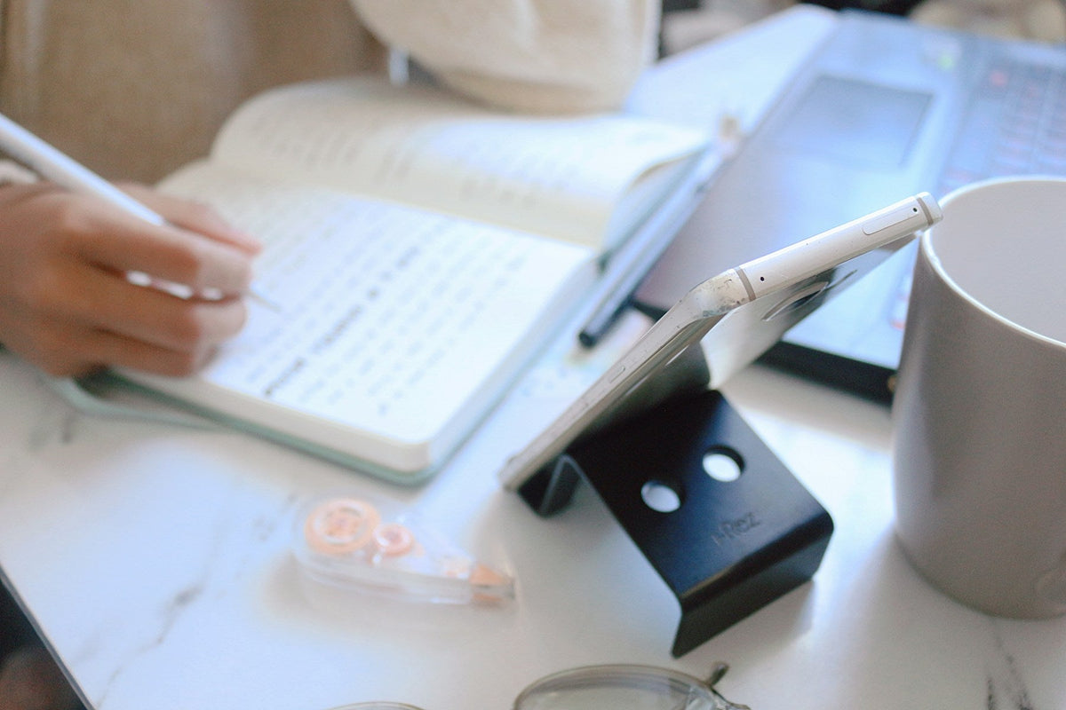 Person writing in a notebook beside a laptop